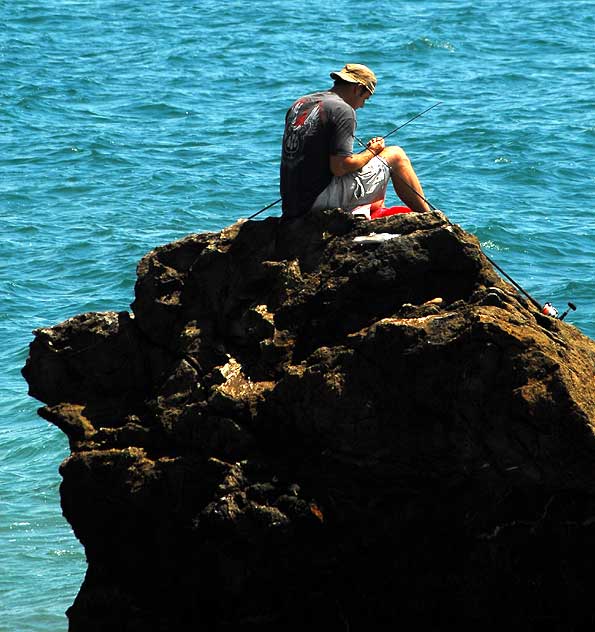 Man fishing from large rock just off the beach in Malibu, near Topanga Canyon 