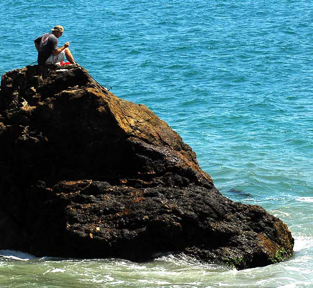 Man fishing from large rock just off the beach in Malibu, near Topanga Canyon 