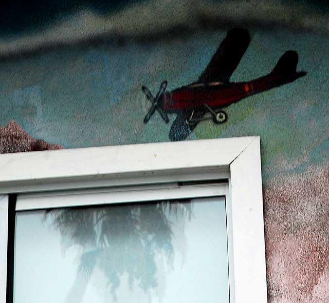 Airplane painted on wall, palm reflected in window