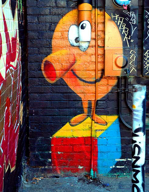 Graffiti on alley wall behind Melrose Avenue - orange man on multi-colored box 