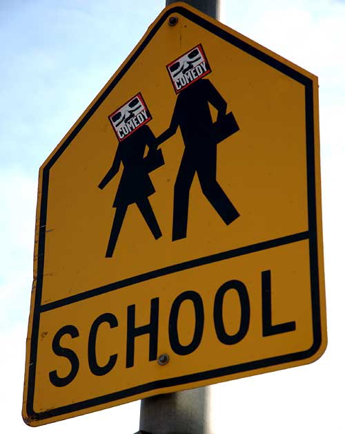 School crossing sign with comedy stickers on Highland Avenue, at Hollywood High School