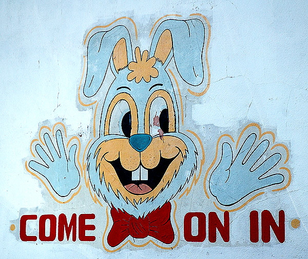 Rabbit graphic with disembodied blue hands on cracked stucco wall, used car lot, Santa Monica Boulevard between Gower and Vine