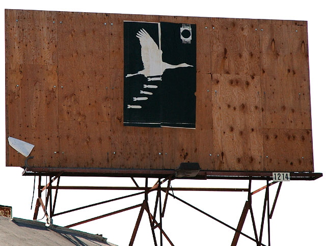Stork dropping bombs poster on wooden billboard, Melrose Avenue