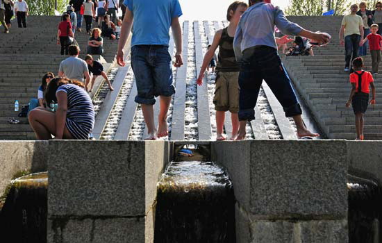 Inside the park, at the right bank end of the footbridge; there is a waterfall that steps down steps. Somebody went to a lot of trouble to turn some boring granite stairs into a place where kids can play, always at the risk of falling down and bruising their scrawny necks.